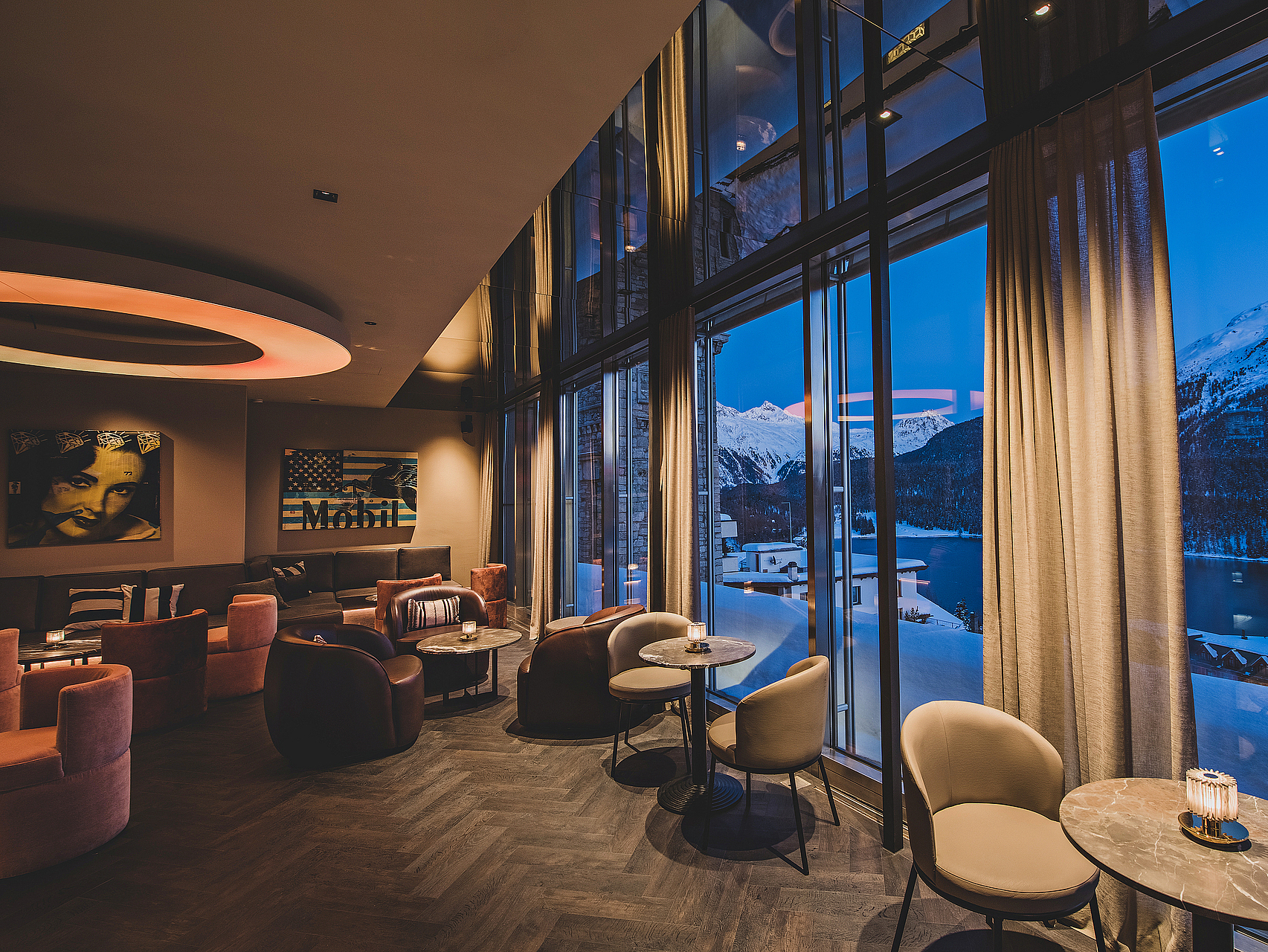 Elegante Bar mit Bergblick in der Dämmerung Elegante Bar mit großen Fenstern, die verschneite Berge und einen See in der Dämmerung zeigen.
