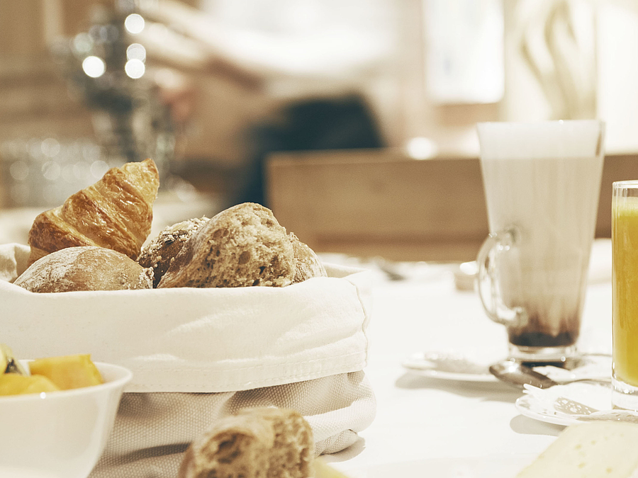 Frühstückstisch mit Brotkorb, Orangensaft und Latte Macchiato.
