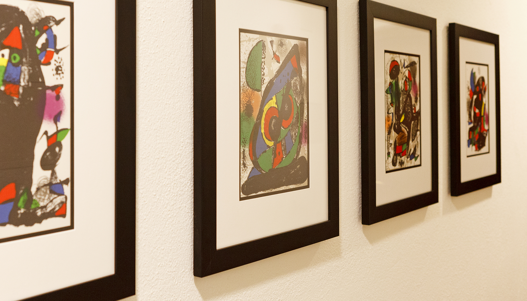 Gerahmte Kunstwerke an Galeriewand Vier gerahmte abstrakte Kunstdrucke hängen in einer Reihe an einer weißen Wand.