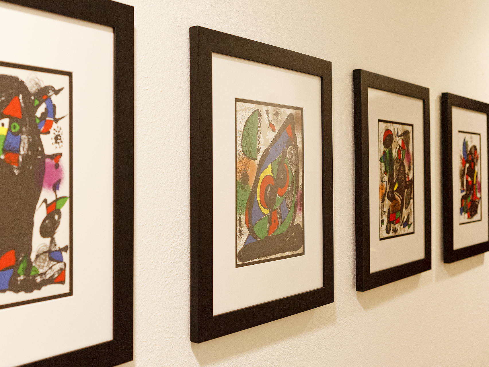 Gerahmte Kunstwerke an Galeriewand Vier gerahmte abstrakte Kunstdrucke hängen in einer Reihe an einer weißen Wand.