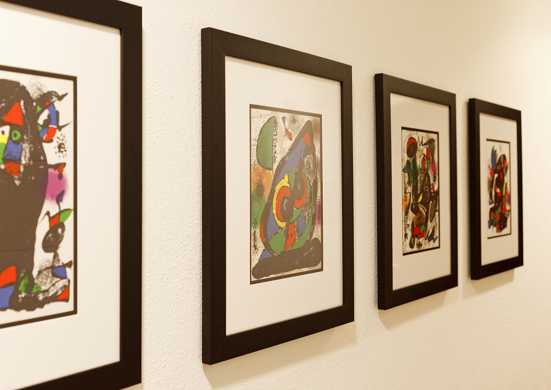 Gerahmte Kunstwerke an Galeriewand Vier gerahmte abstrakte Kunstdrucke hängen in einer Reihe an einer weißen Wand.
