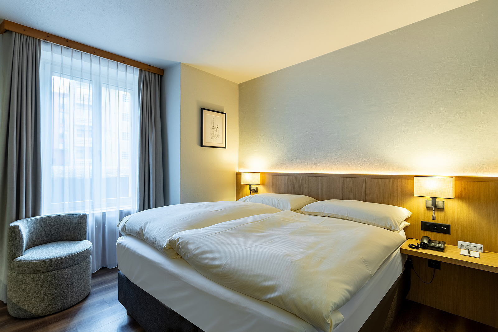 Gemütliches Hotelzimmer Ein gemütliches Hotelzimmer mit einem gemachten Doppelbett und einem Sessel am Fenster.