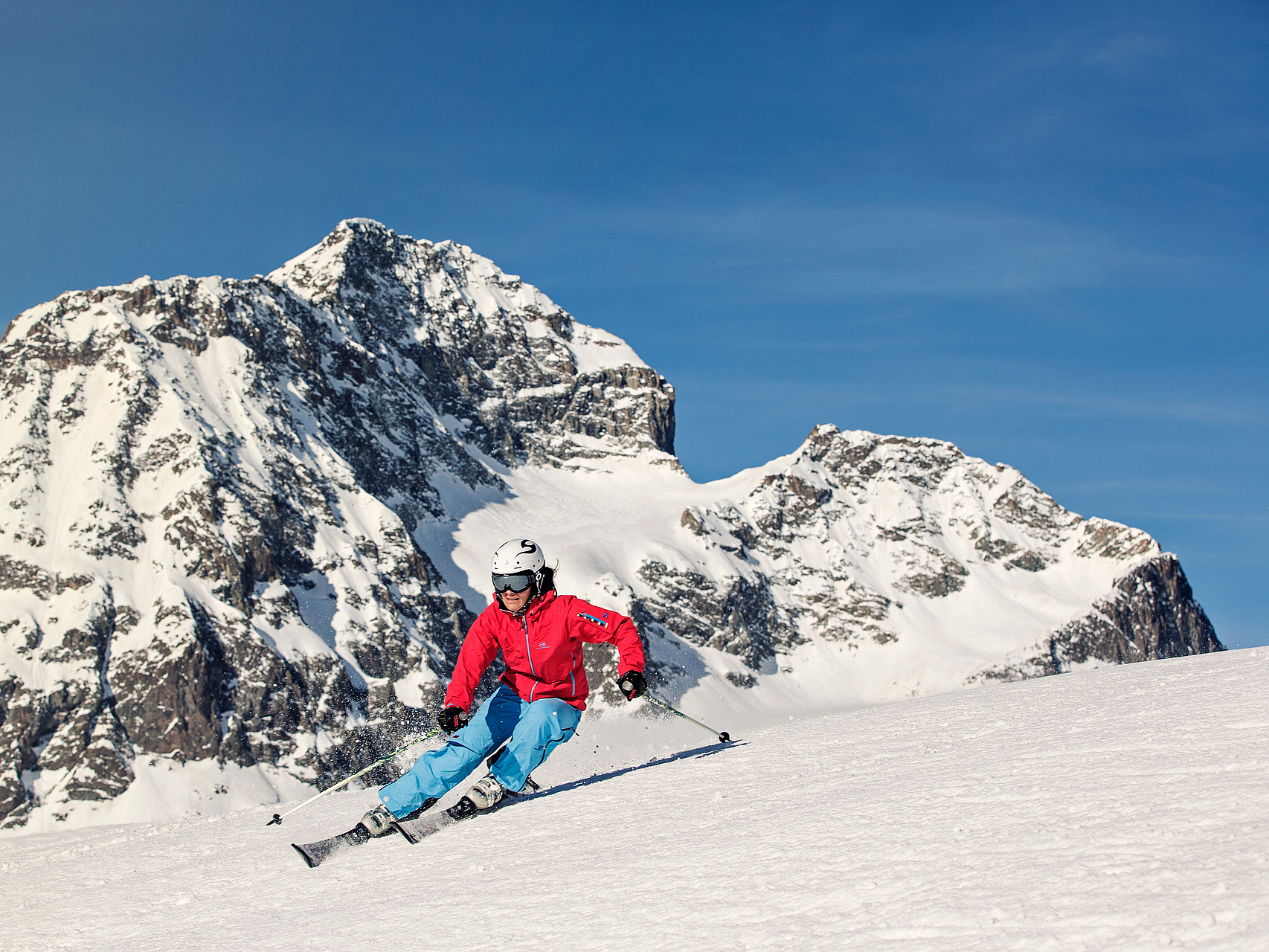 Skifahrer auf verschneiter Piste Skifahrerin auf verschneiter Piste vor Bergpanorama.