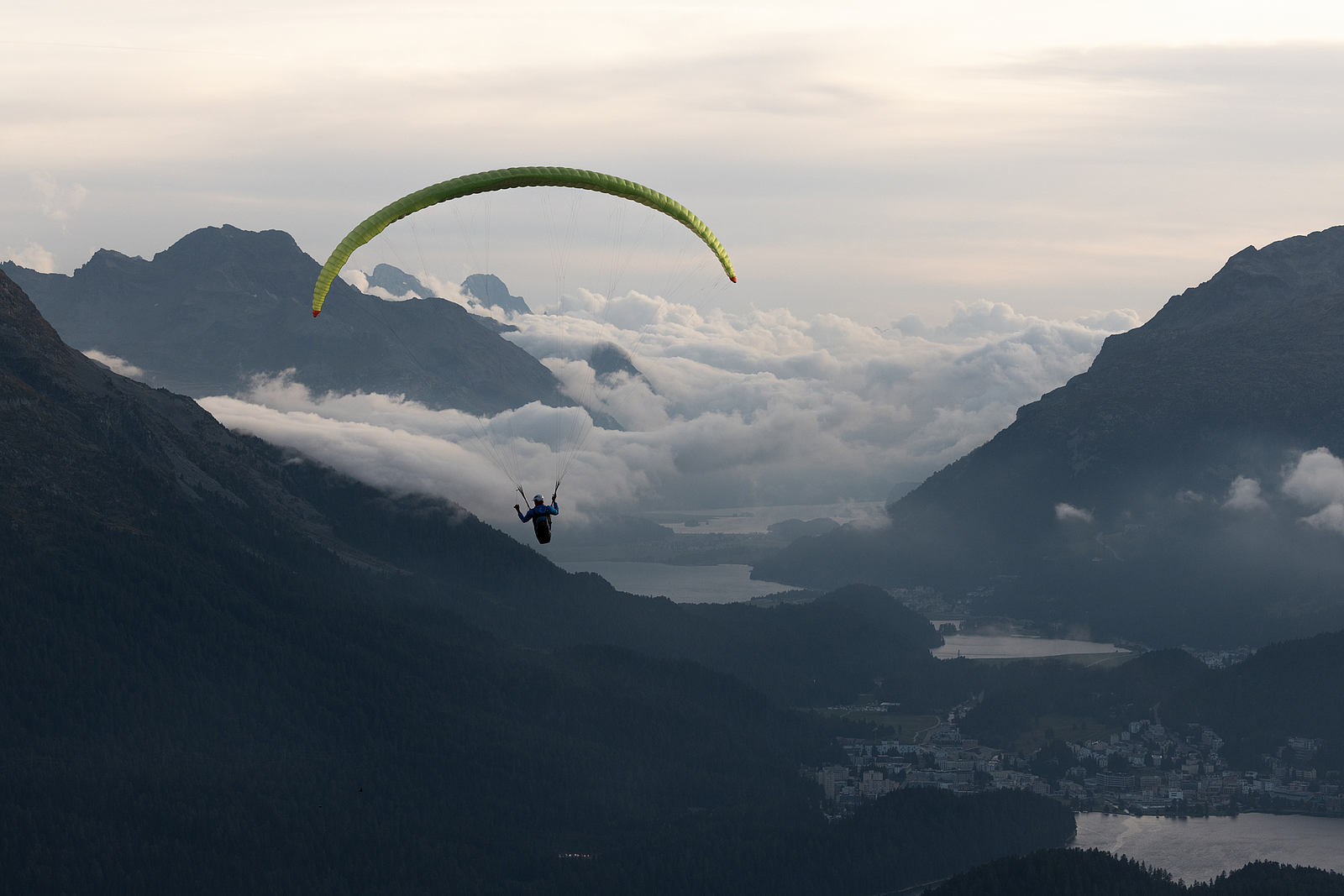 Gleitschirmflieger hoch über Berggipfeln und einem nebligen Alptal.