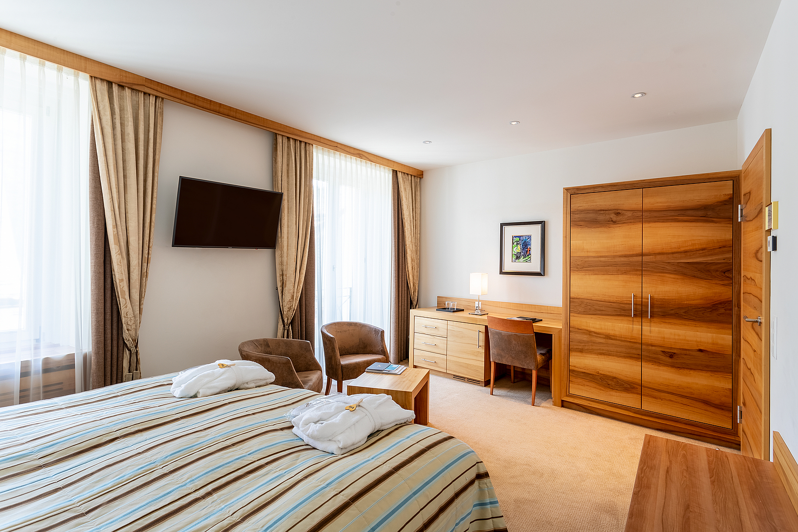 Modernes Hotelzimmer mit Bett, Holzschrank, Schreibtisch und Sesseln.