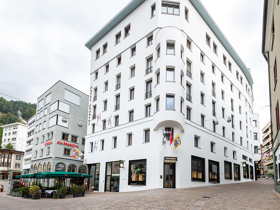 Ein grosses, weisses Hotelgebäude mit geschwungener Architektur und Geschäften im Erdgeschoss in St. Moritz.