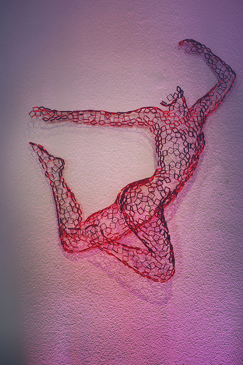 Skulptur eines springenden Tänzers aus rotem Draht auf rosa Wand.