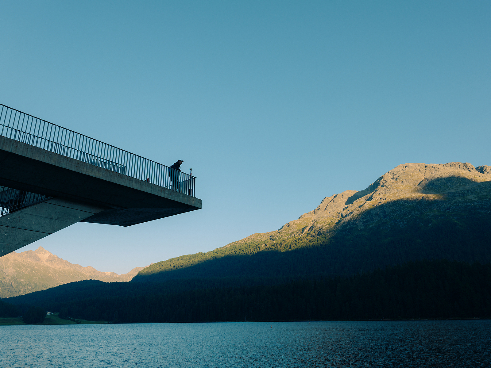 Person auf Aussichtsplattform mit Blick auf See und Berge