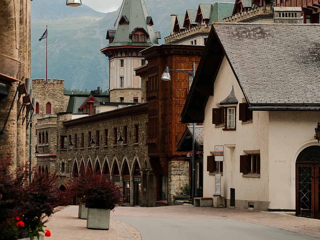 Alpen-Dorfstraße in den Alpen Geschwungene Straße in einem Alpendorf mit historischen Gebäuden und Bergen.