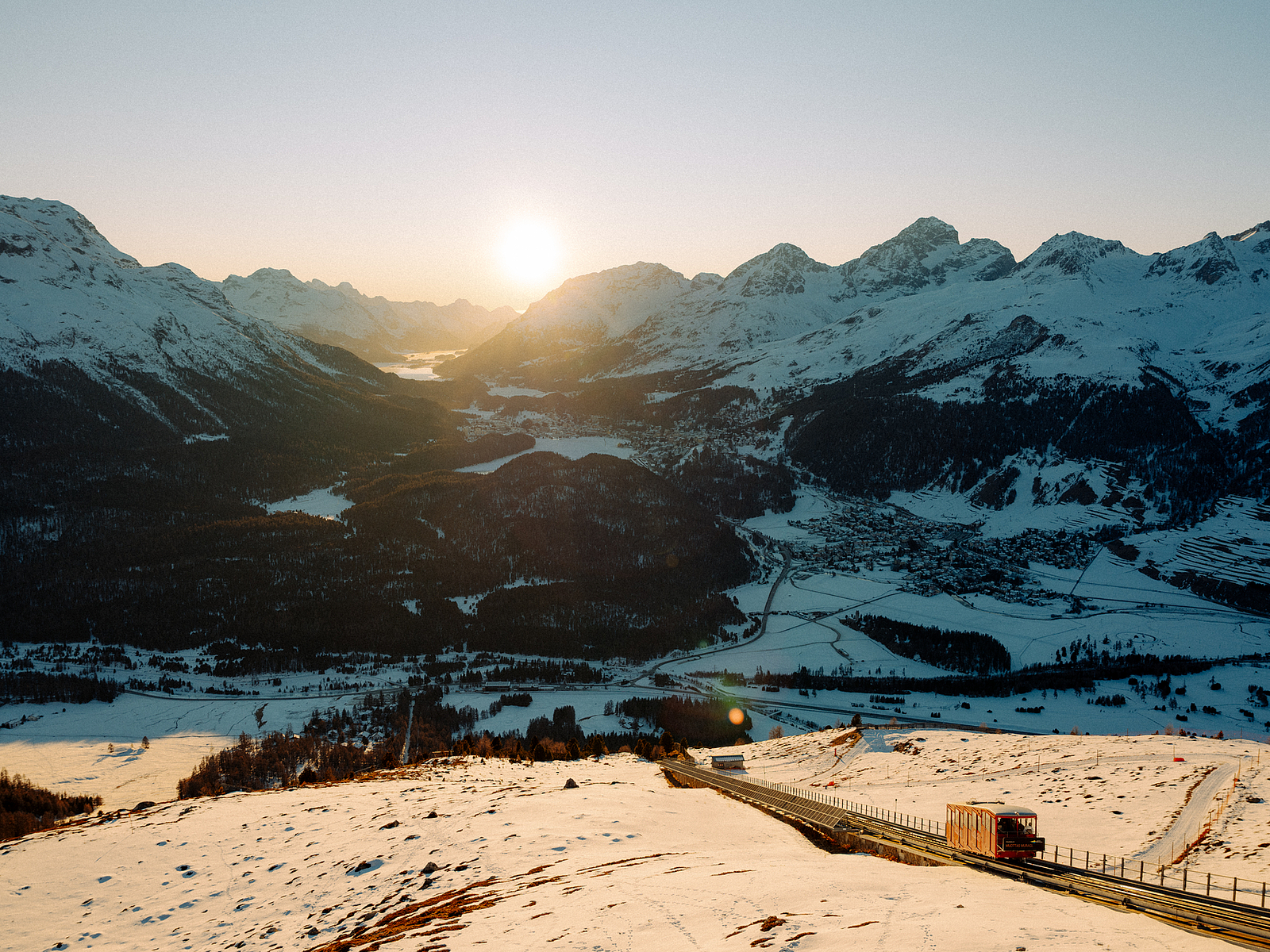 Sonnenuntergang über verschneitem Tal Rote Standseilbahn am verschneiten Hang mit Sonnenuntergang