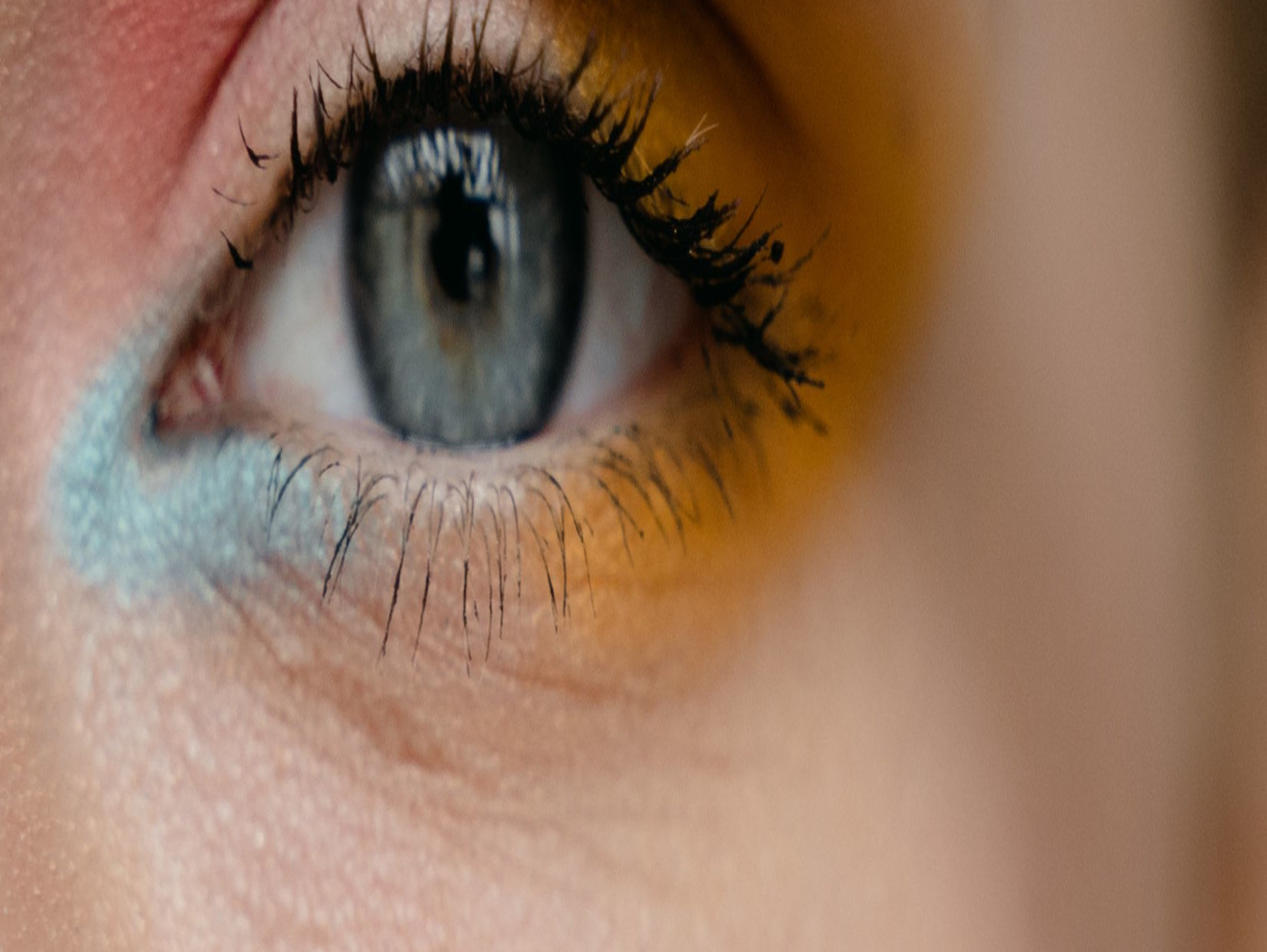 Ein Make-up-Pinsel trägt roten Lidschatten auf ein buntes Augen-Make-up auf.