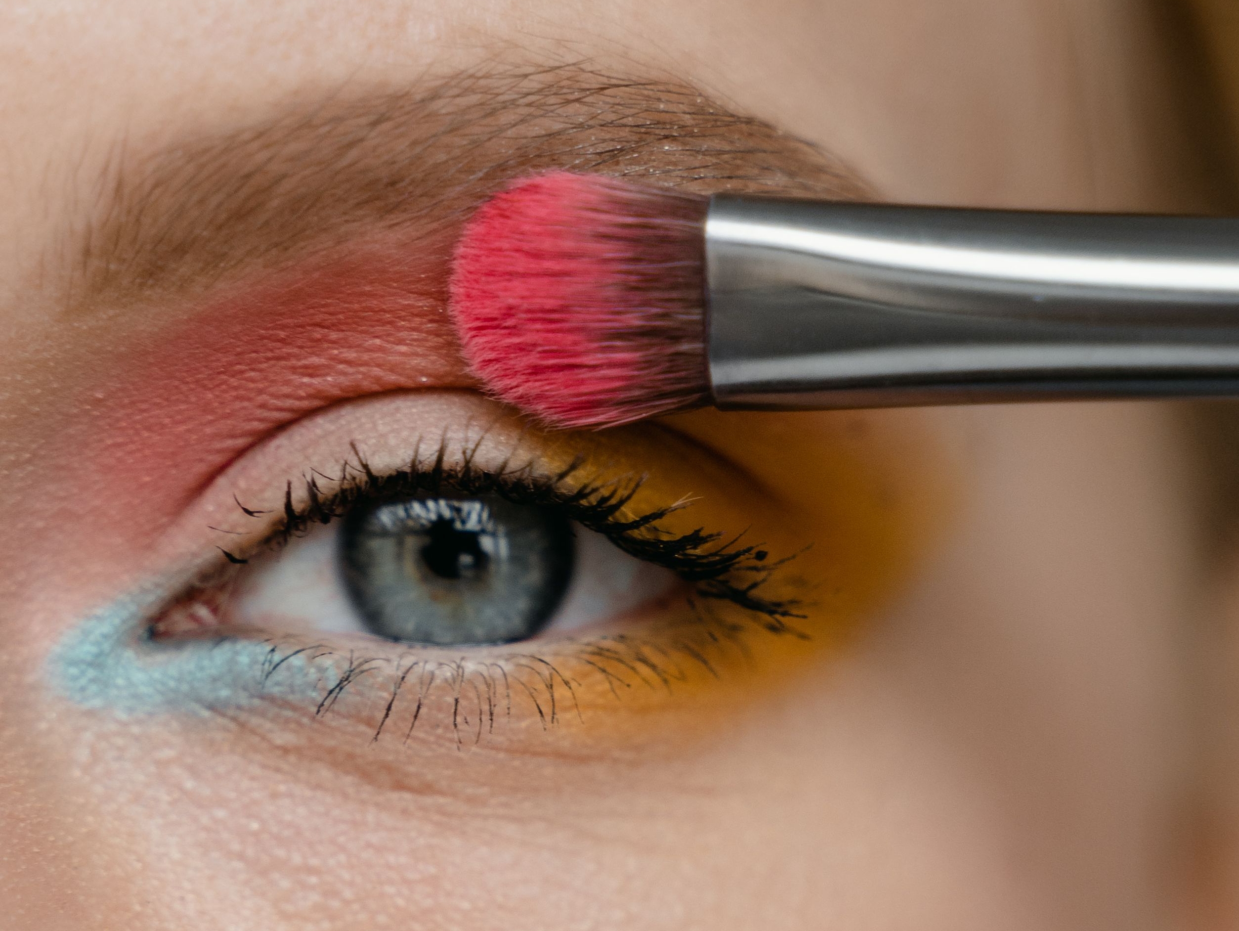 Buntes Augen-Make-up auftragen Ein Make-up-Pinsel trägt roten Lidschatten auf ein buntes Augen-Make-up auf.