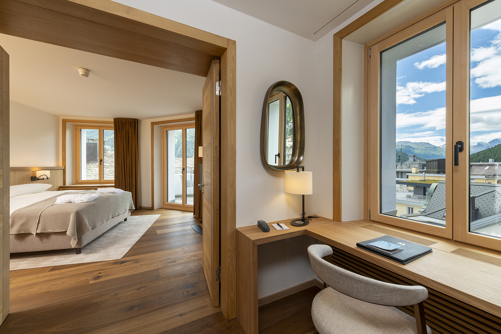 Hotelzimmer mit Holztisch, Spiegel und Blick ins Schlafzimmer.