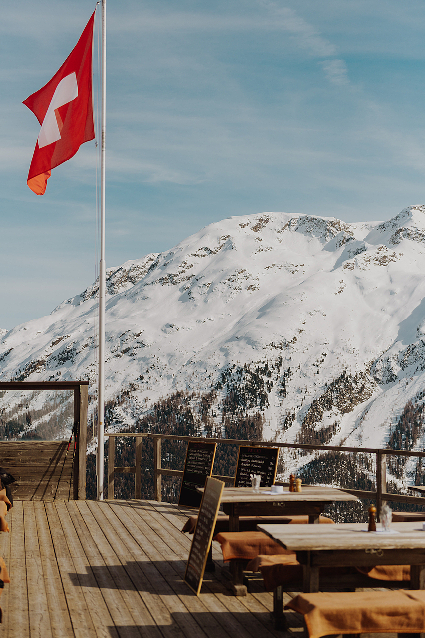 Schweizer Flagge auf Terrasse mit Blick auf verschneite Alpen