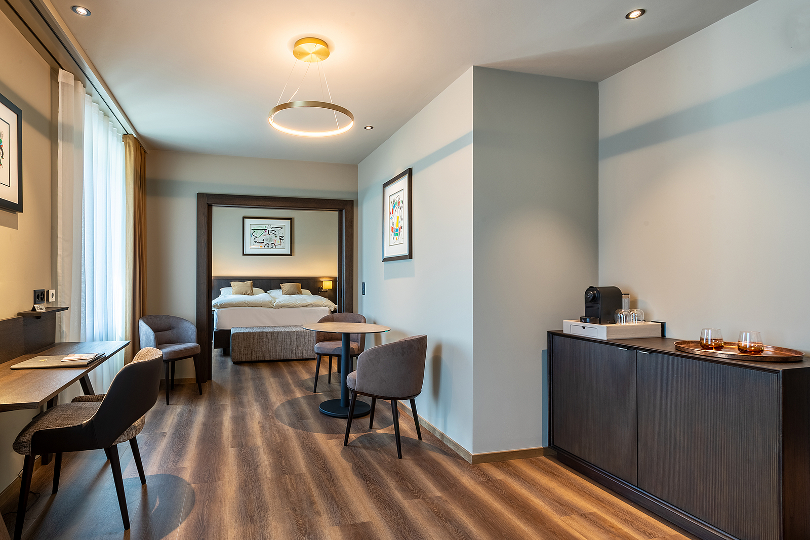 Innenansicht einer modernen Hotelsuite mit Sitzecke und Schlafzimmer.