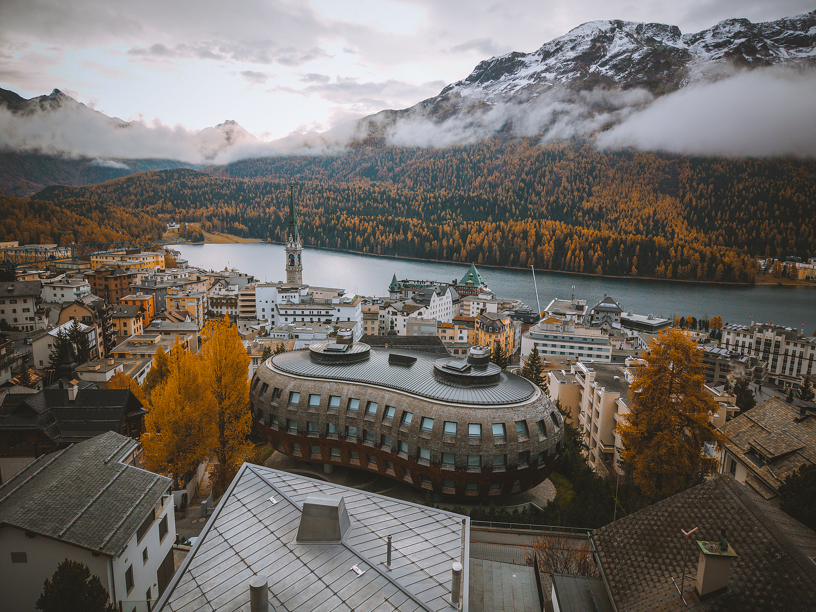 Bergort im Herbst Alpenort mit See, Herbstwald und verschneiten Bergen.
