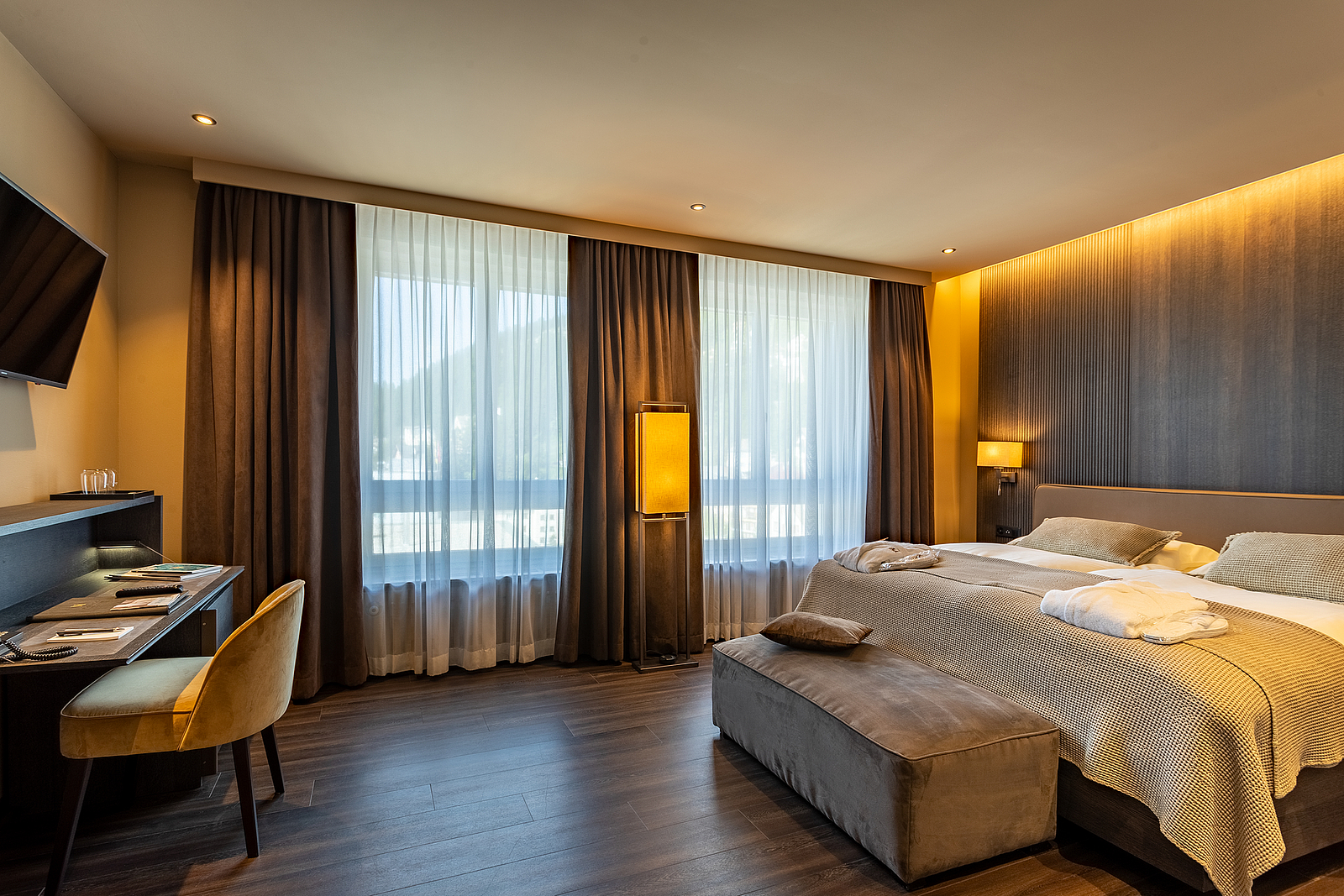 Luxuriöses Hotelzimmer Luxuriöses Hotelzimmer mit gemütlichem Bett, Bank, großen Fenstern und Schreibtisch.