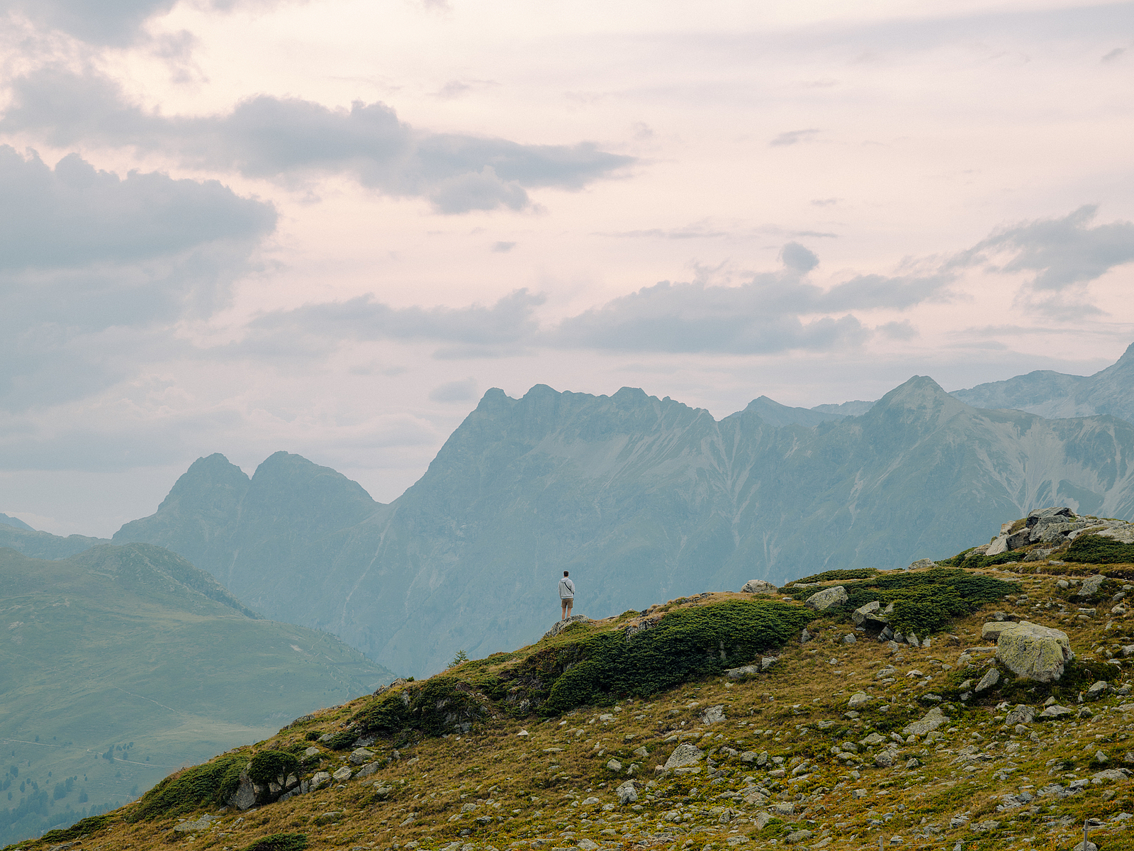 Ein Wanderer auf einem grünen Bergrücken mit Blick auf ferne Gipfel.
