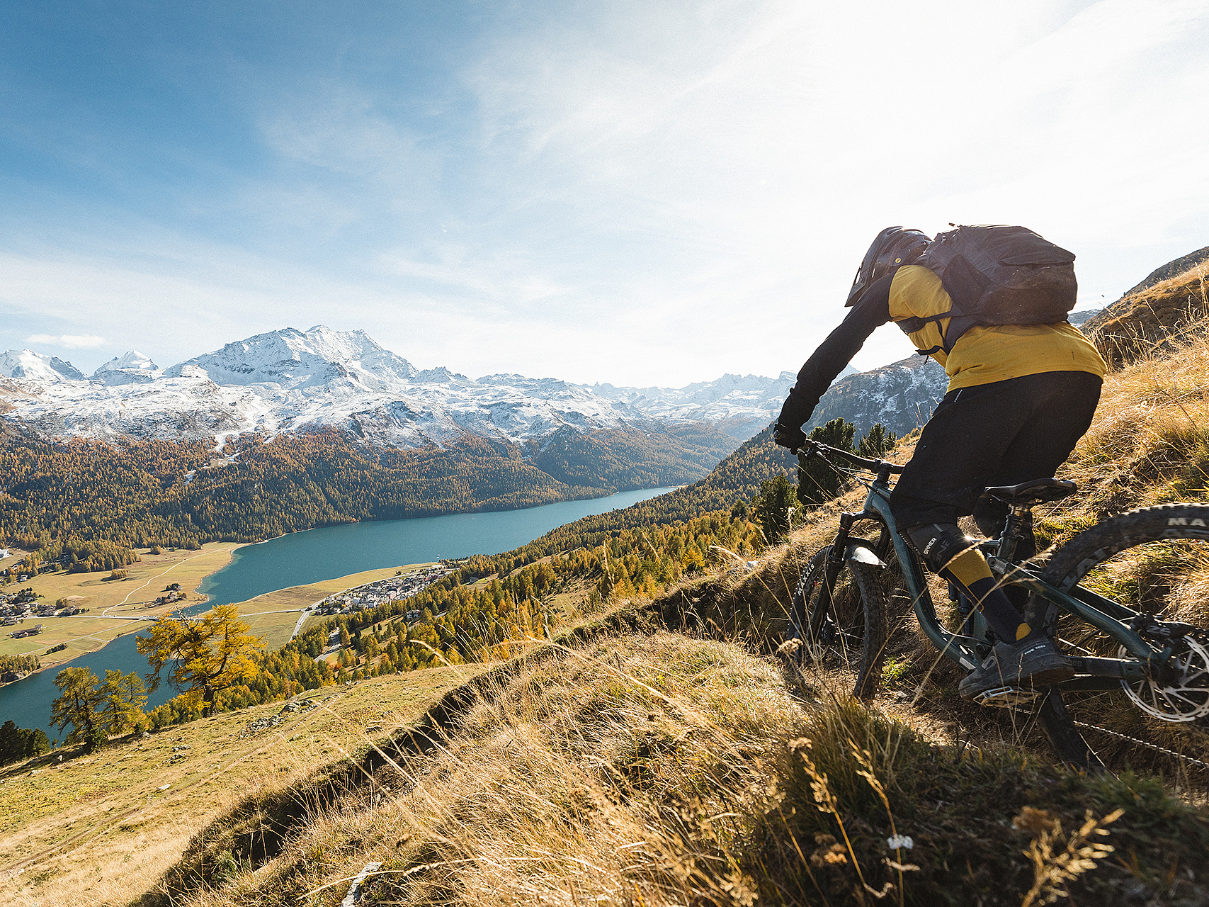 Mountainbiker in den Alpen Ein Mountainbiker auf einem steilen Alpinen Trail mit Blick auf See und schneebedeckte Berge.