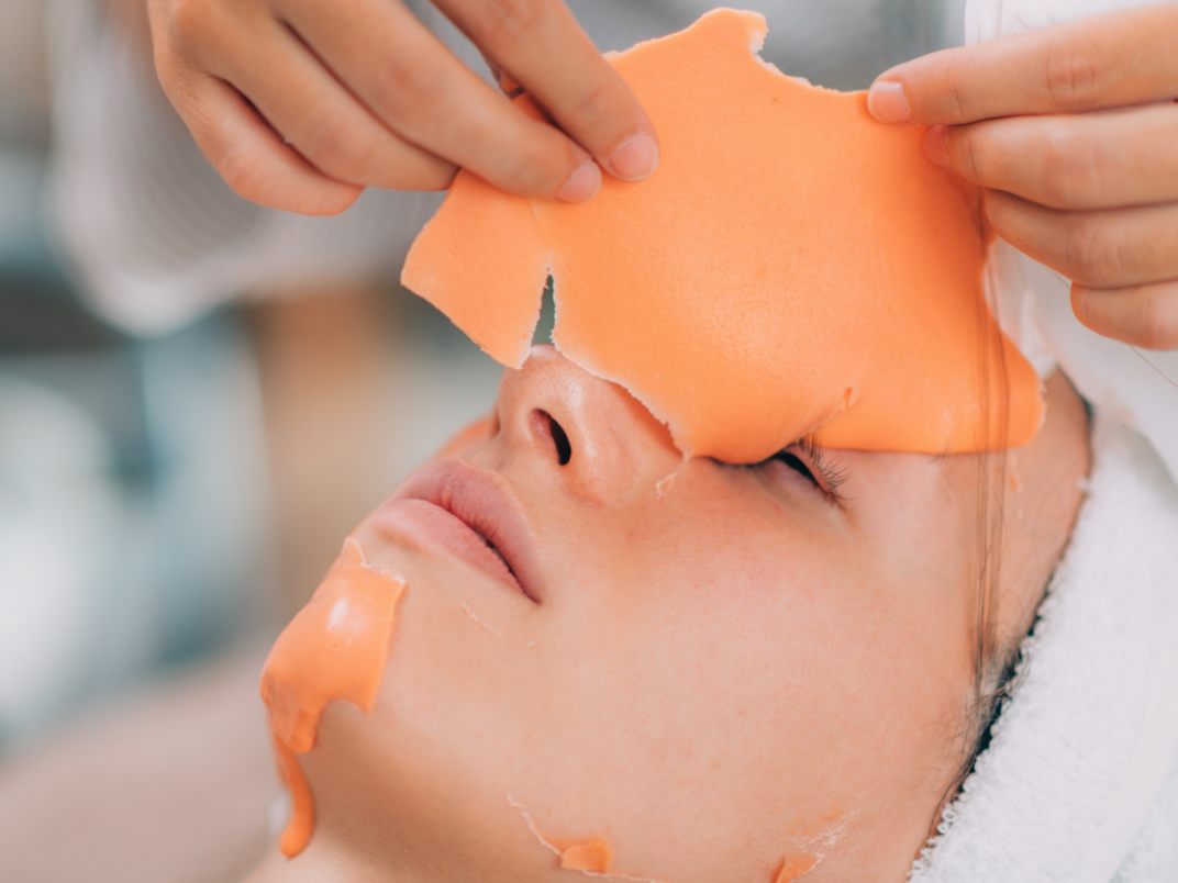 Peel-off Gesichtsmasken-Behandlung Kosmetikerin zieht orangefarbene Maske vom Gesicht.