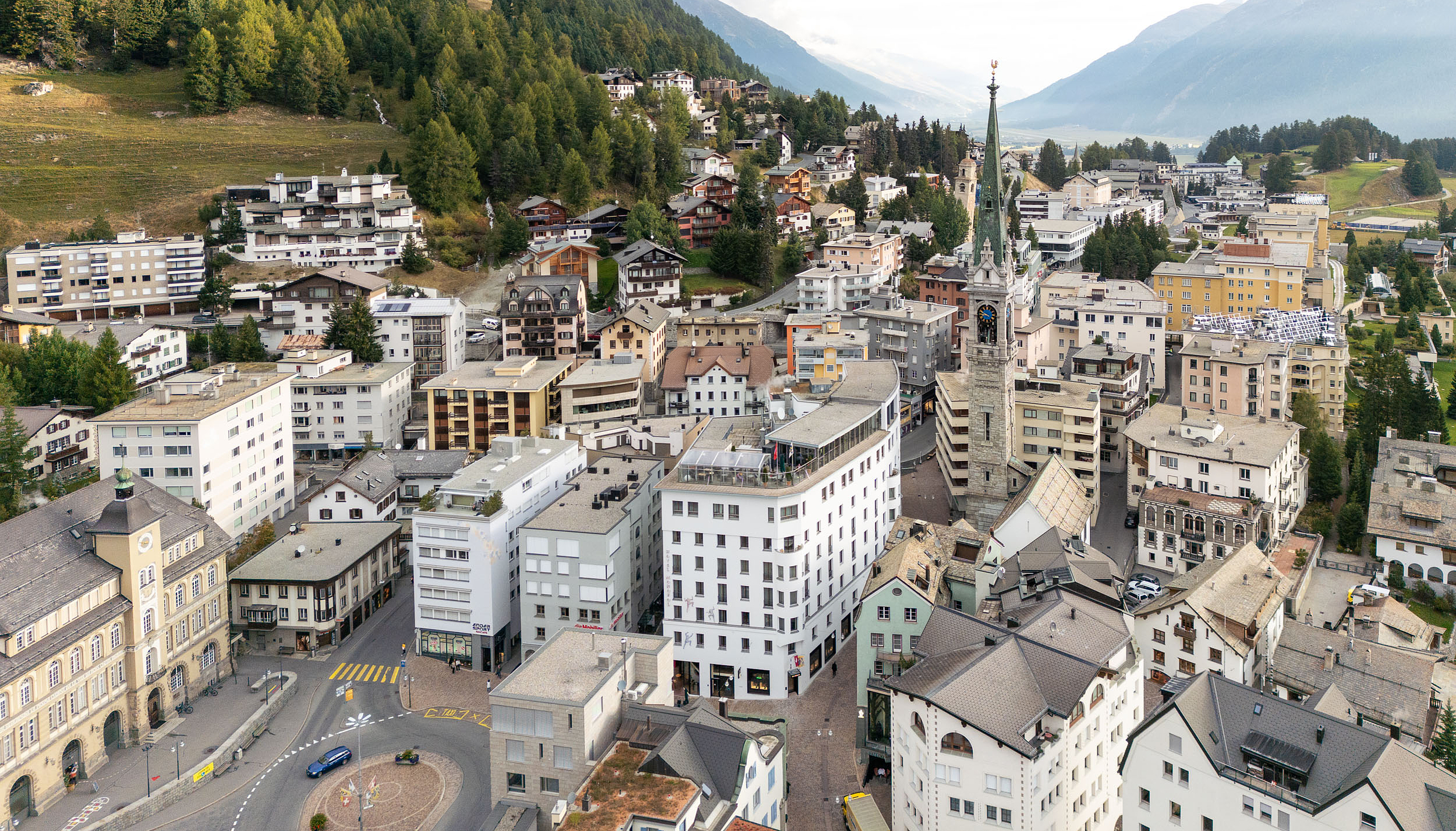Malerischer Bergort Blick Luftaufnahme eines Bergdorfes mit Kirchturm und bewaldeten Hügeln.