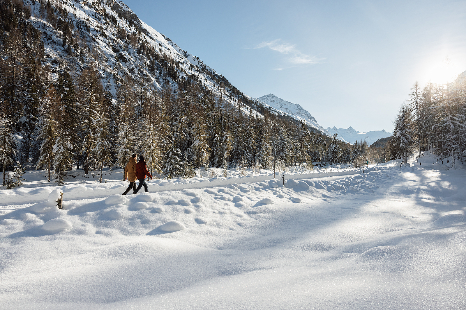 Zwei Personen wandern auf einem verschneiten Weg in den österreichischen Alpen.