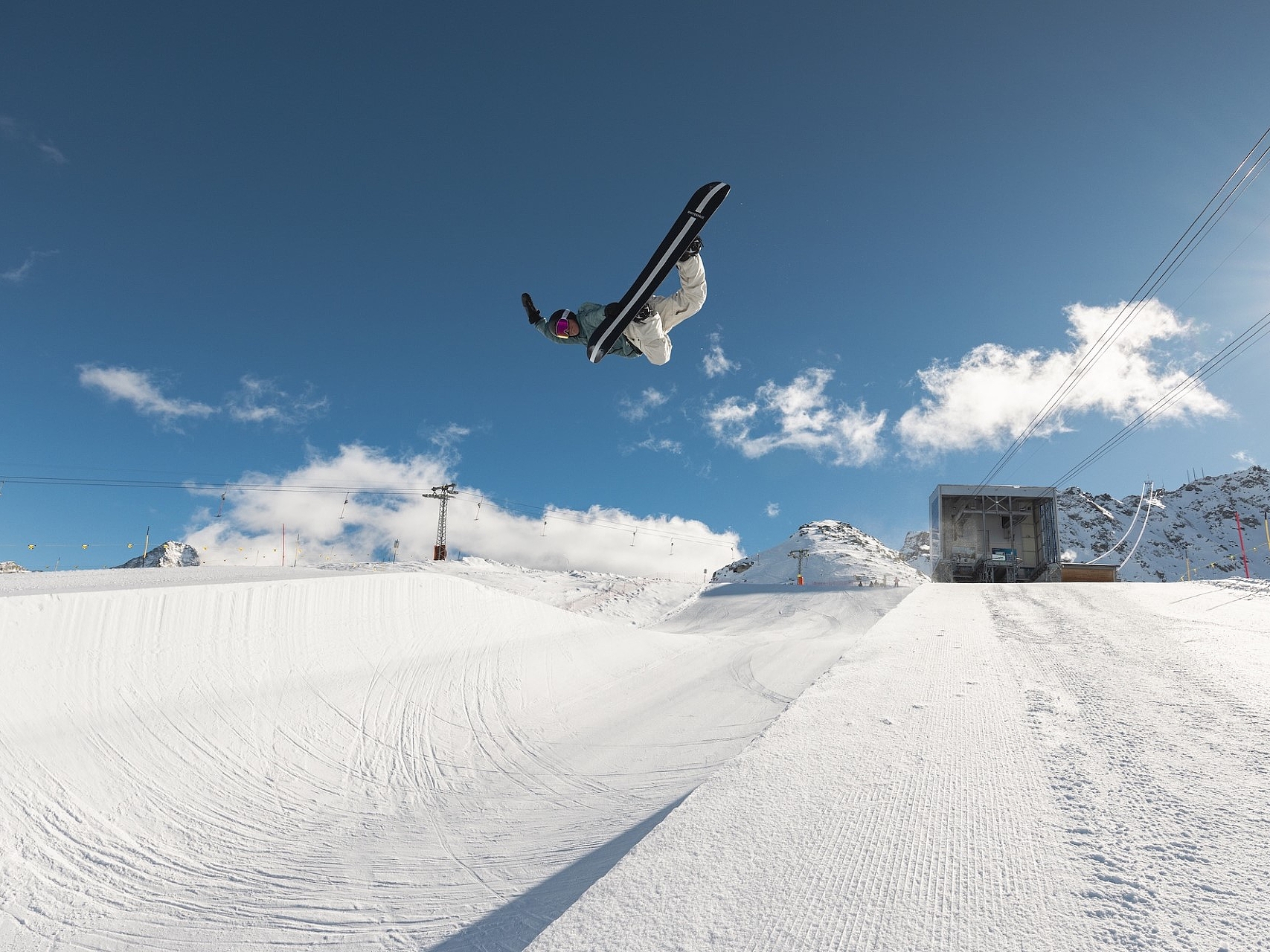 Snowboarder in Aktion Ein Snowboarder macht einen hohen Sprung über eine Halfpipe in einem verschneiten Skigebiet.