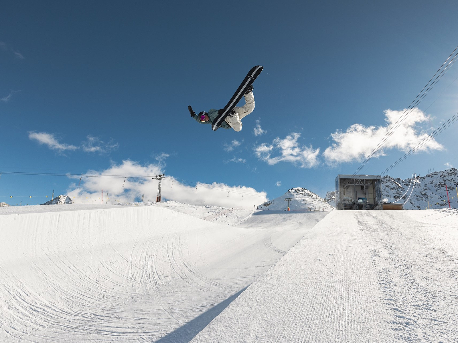 Snowboarder in Aktion Ein Snowboarder macht einen hohen Sprung über eine Halfpipe in einem verschneiten Skigebiet.