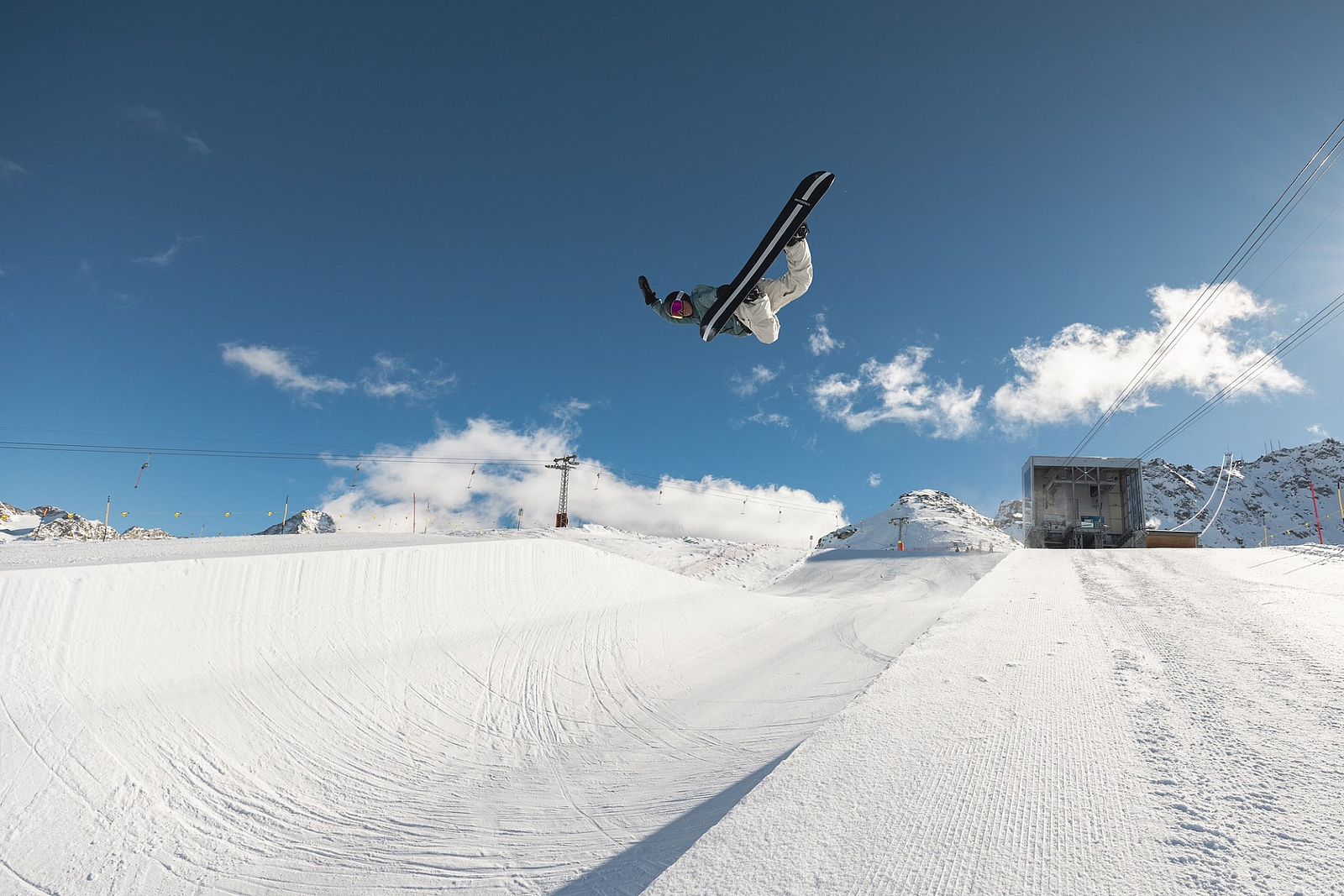 Ein Snowboarder macht einen hohen Sprung über eine Halfpipe in einem verschneiten Skigebiet.