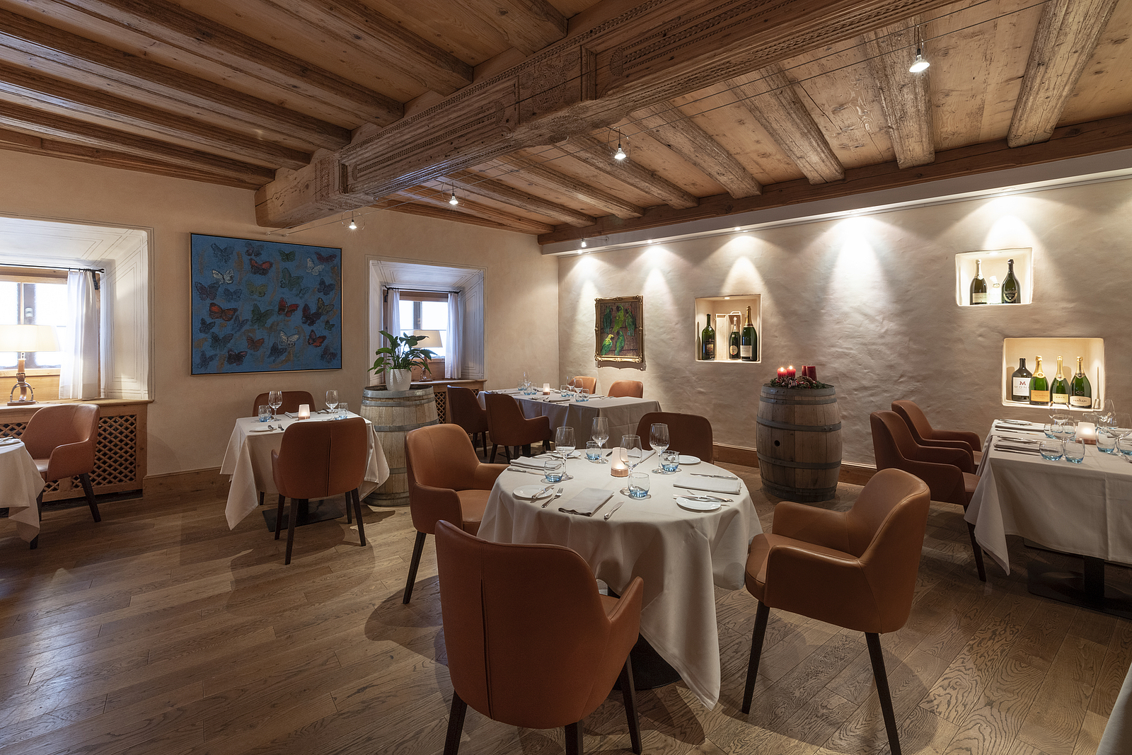 Rustikales Restaurant mit Holzbalken, weiß gedeckten Tischen und braunen Ledersesseln