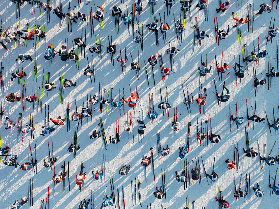 Luftaufnahme von Skilangläufern Viele Skilangläufer im Schnee mit langen Schatten von oben.
