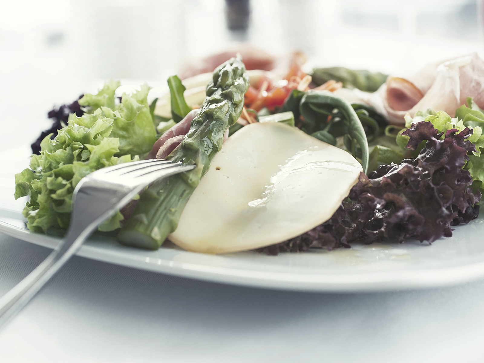 Frischer Salat mit Spargel, Käse und Schinken auf einem Teller mit Gabel.