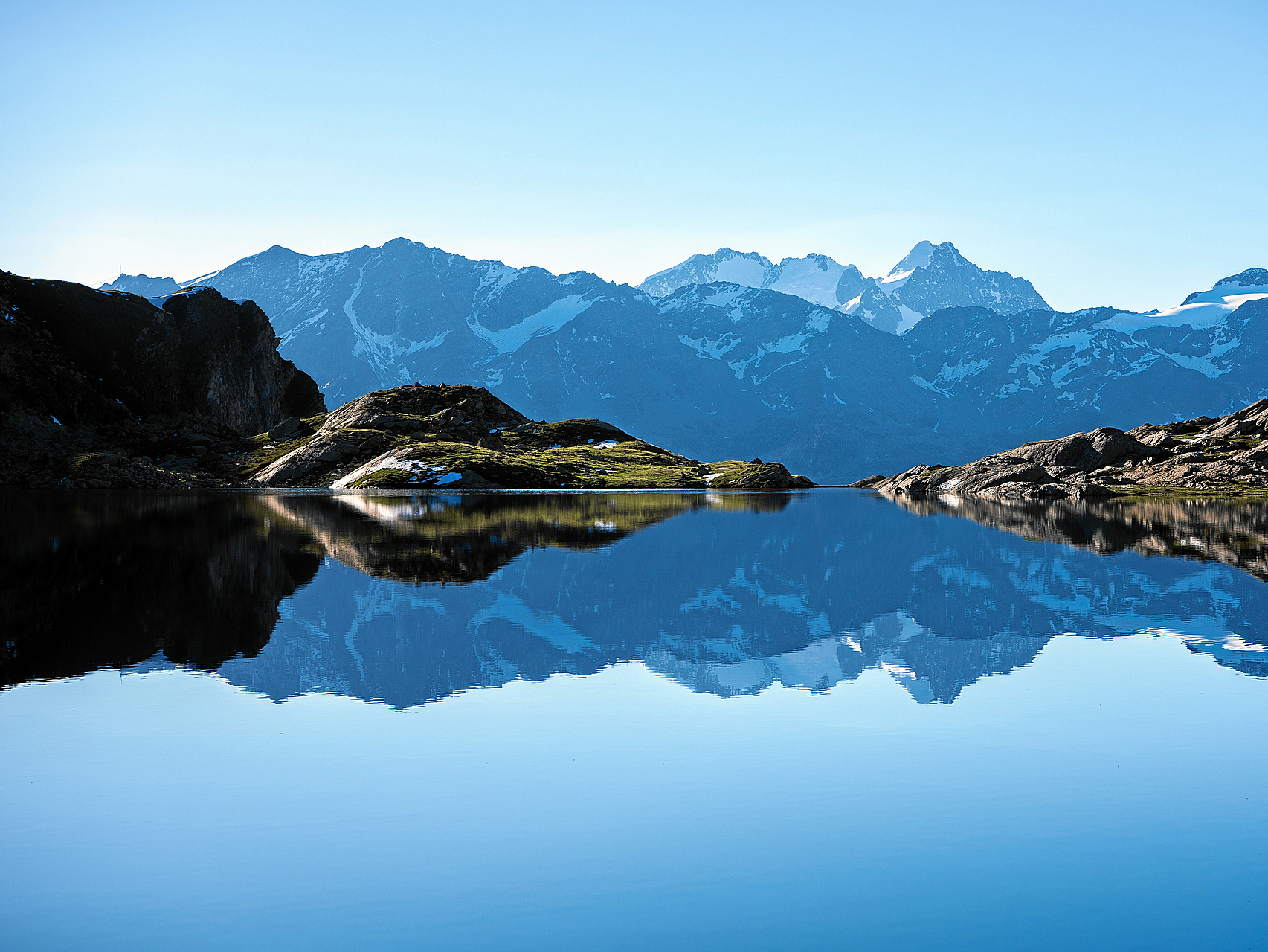 Bergsee Spiegelung Ruhiger Bergsee, der majestätische, schneebedeckte Berge und blauen Himmel spiegelt.