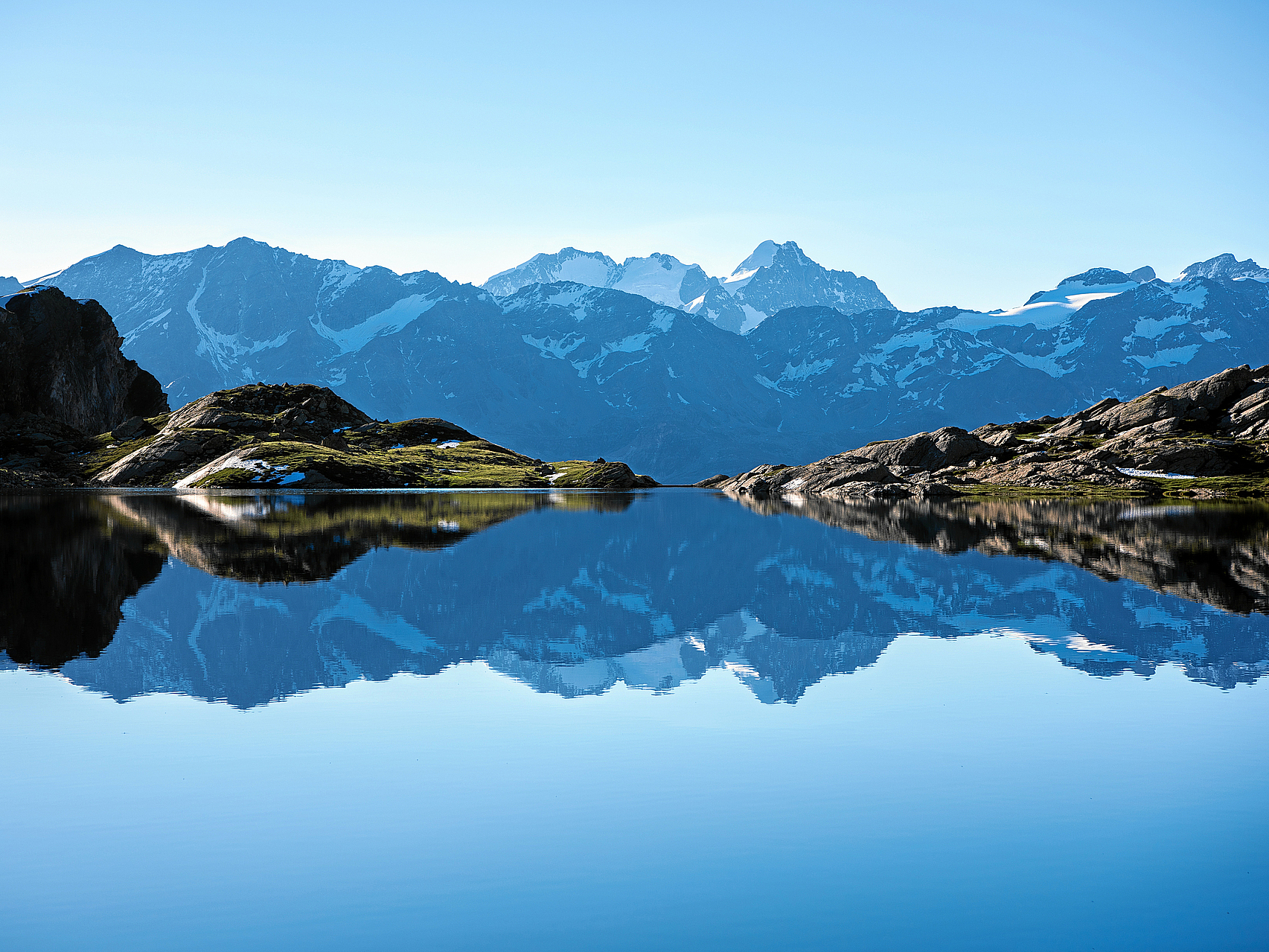 Bergsee Spiegelung Ruhiger Bergsee, der majestätische, schneebedeckte Berge und blauen Himmel spiegelt.