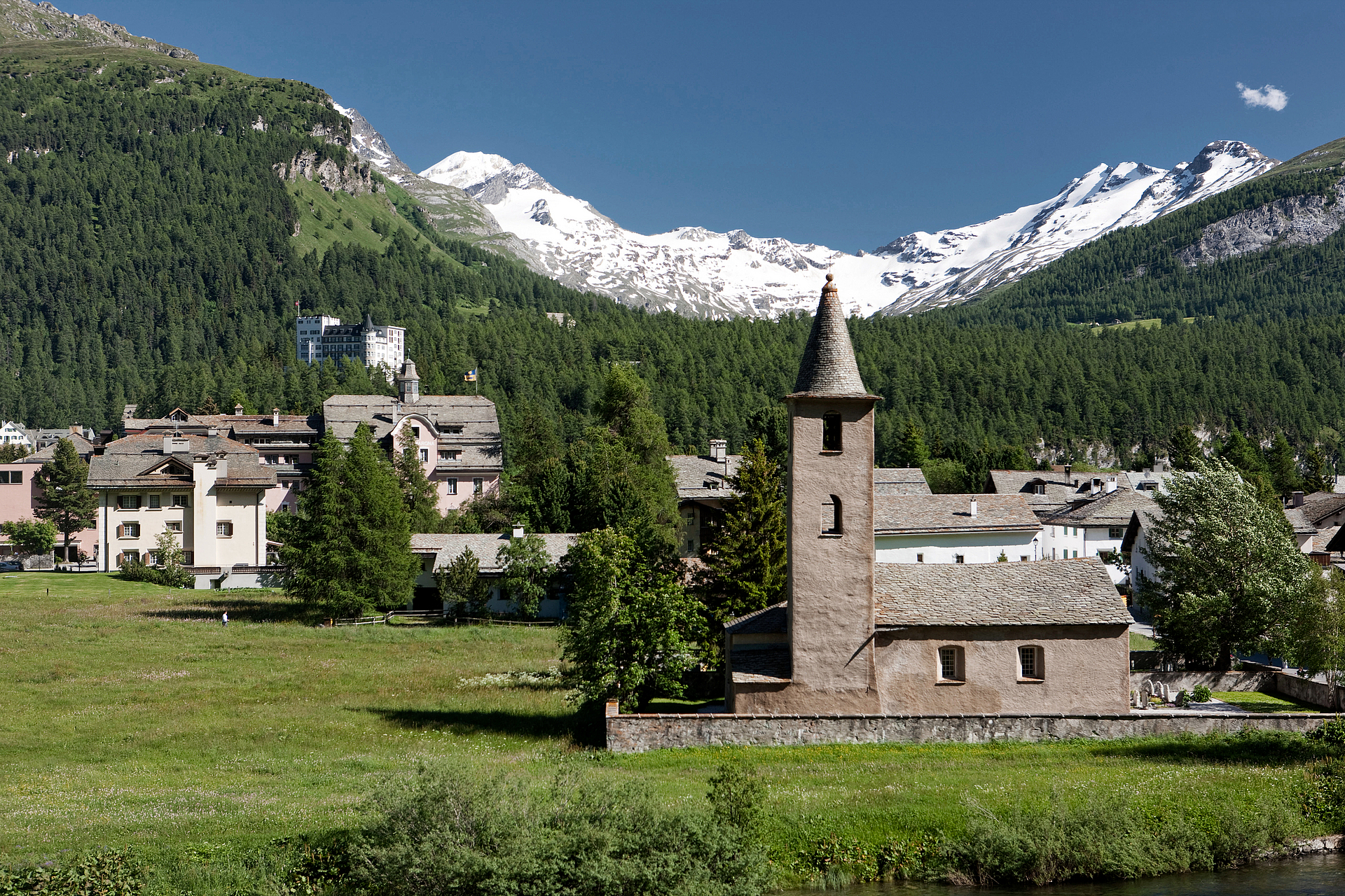 Alpendorf mit Kirche und schneebedeckten Bergen Alpendorf mit historischer Steinkirche und schneebedeckten Bergen im Hintergrund.