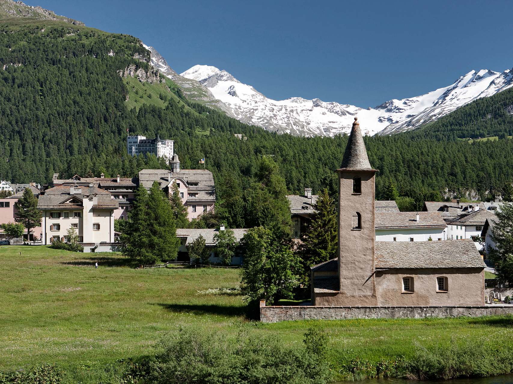Alpendorf mit Kirche und schneebedeckten Bergen Alpendorf mit historischer Steinkirche und schneebedeckten Bergen im Hintergrund.