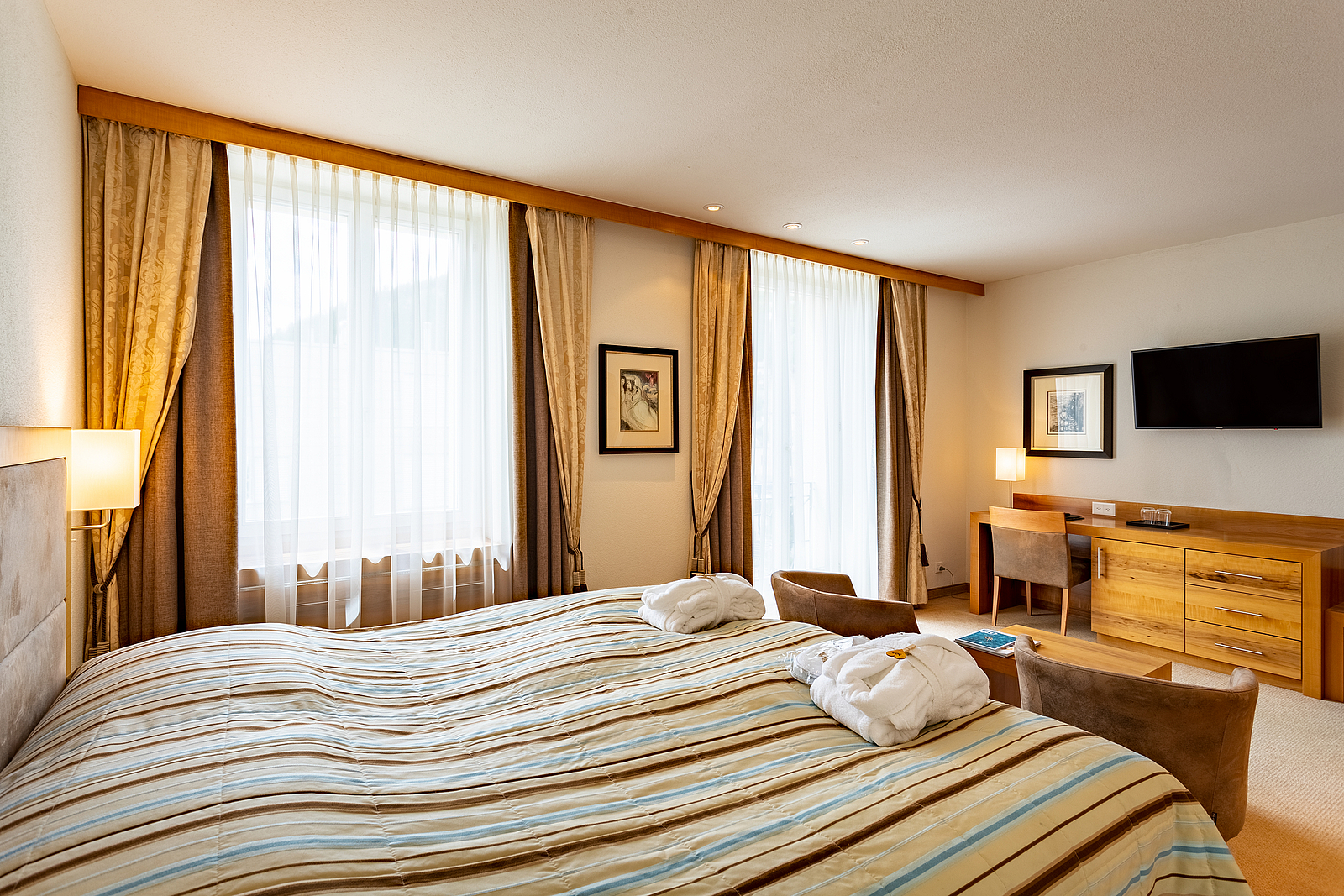 Helliges Hotelzimmer mit gemachtem Bett, Bademänteln und Fenstern.