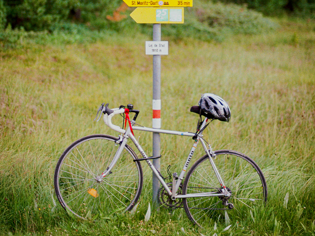 Rennrad an Wegweiser in der Schweiz Silbernes Rennrad lehnt an gelbem Wanderwegweiser auf einer Wiese