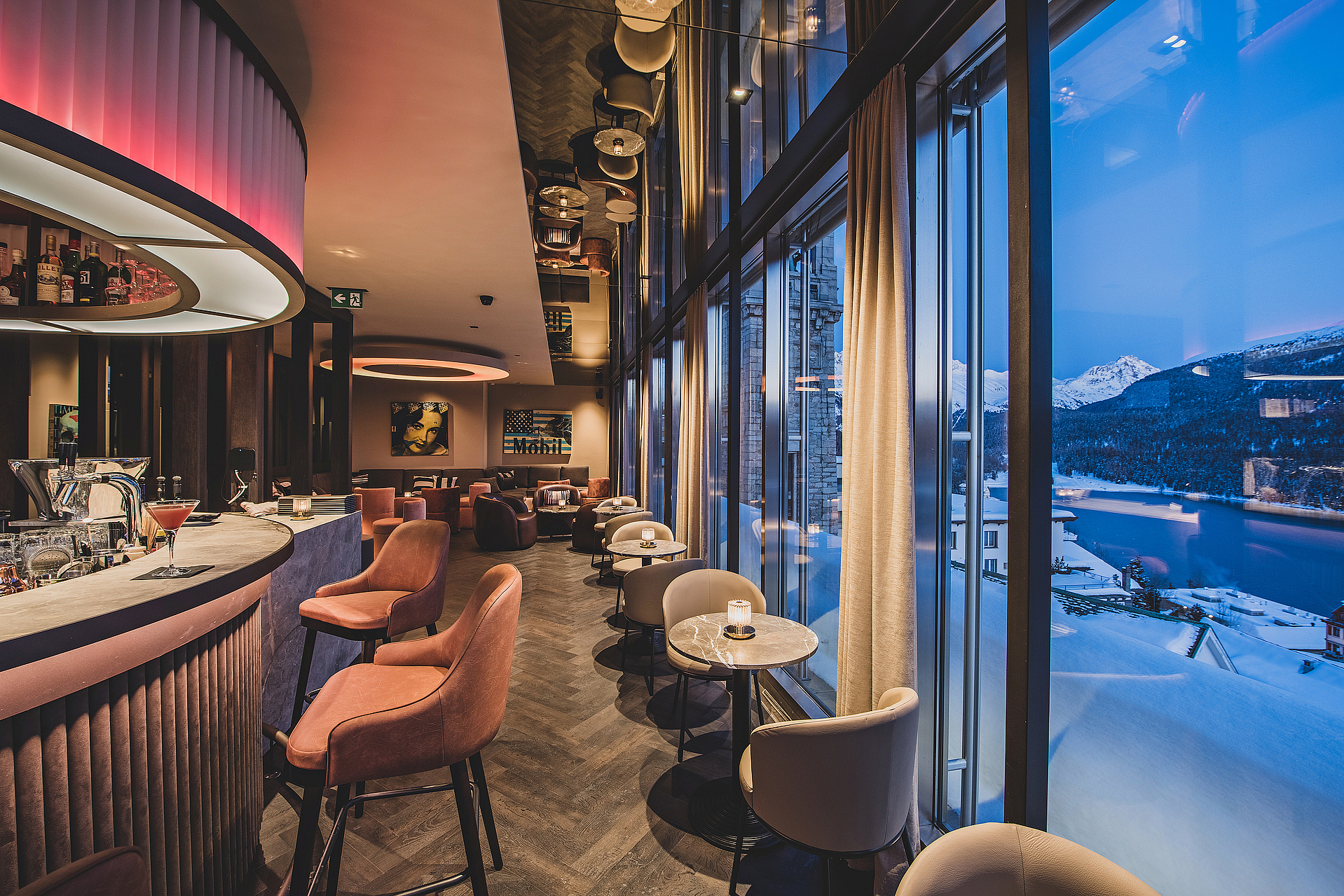Stilvolles Bar-Interieur mit rosa Barhockern und Blick auf eine schneebedeckte Berglandschaft.