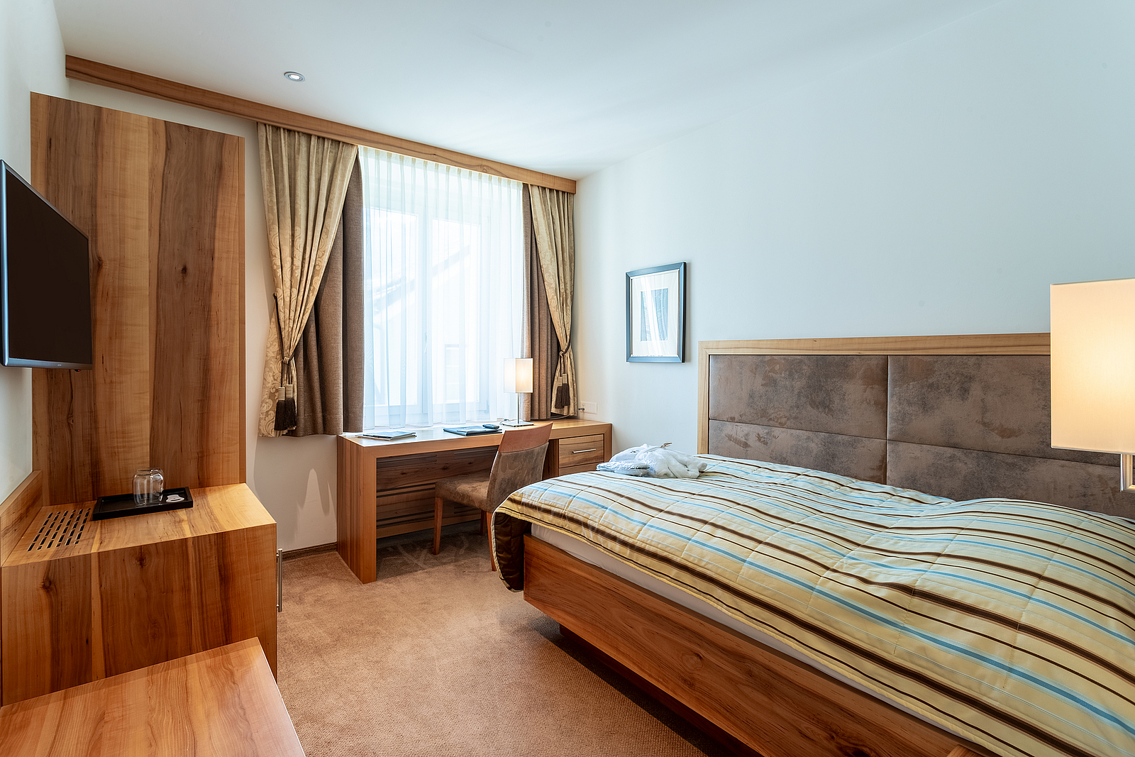 Hotelzimmer mit Einzelbett, Schreibtisch und Holzmöbeln.