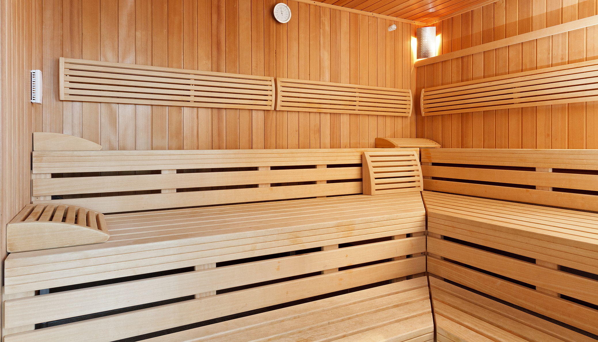 Innenraum einer modernen Holzsauna mit Bänken und Thermometer.
