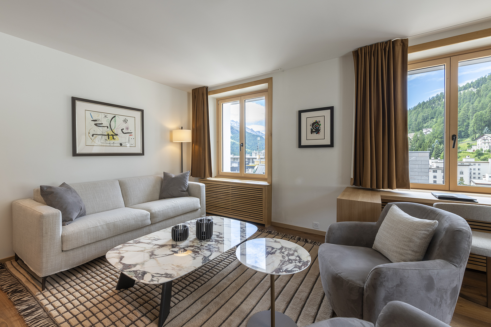Helles Wohnzimmer mit Sofa, Sesseln, Marmortischen und Fenstern mit Bergblick.