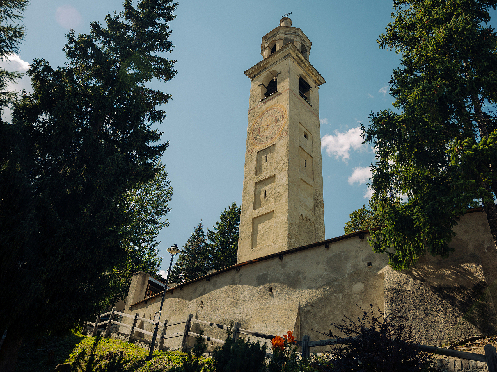 Historischer Kirchturm im Bergdorf Historischer Kirchturm eingerahmt von Bäumen und einer Steinmauer.