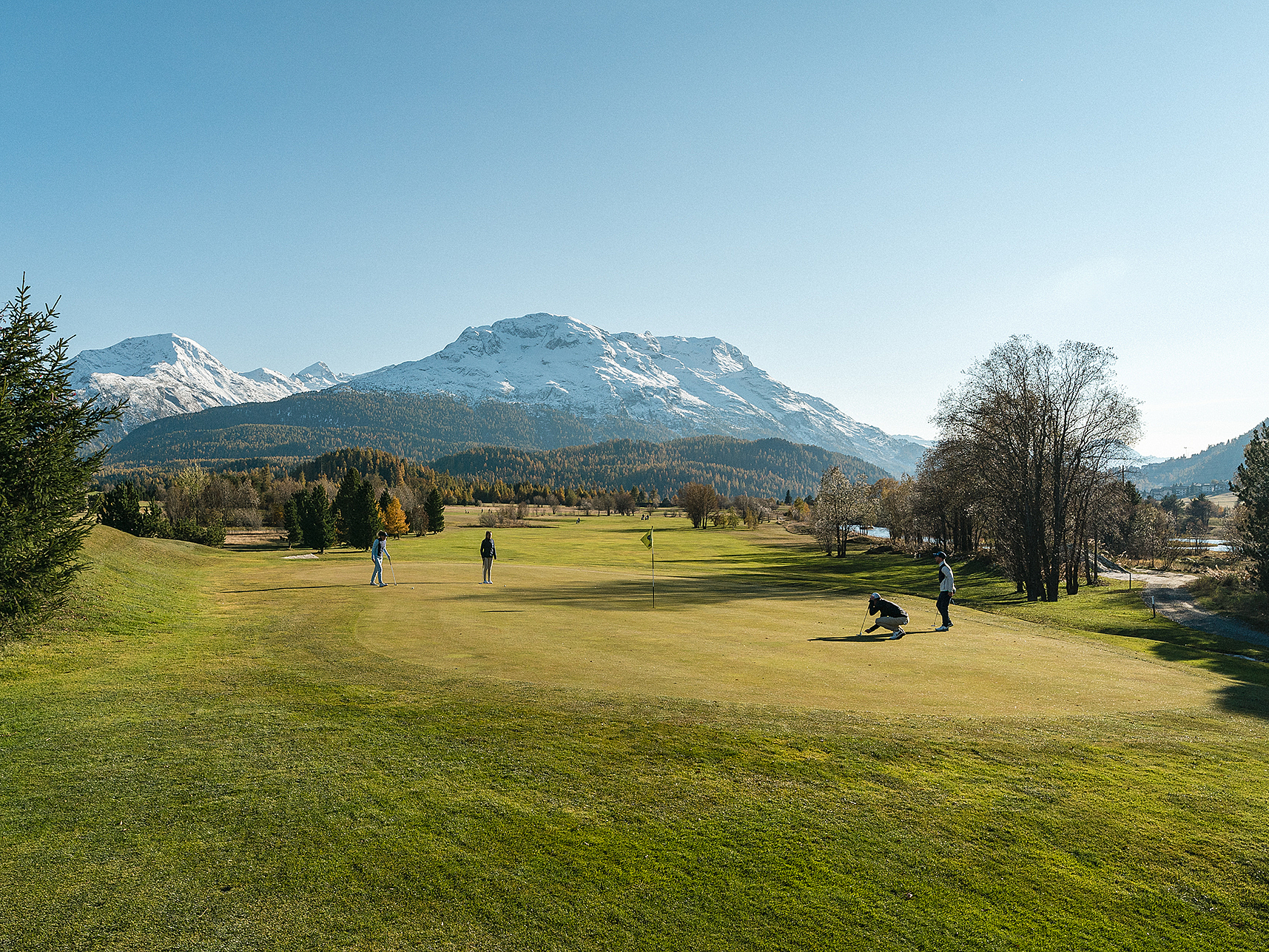 Golfen in den Schweizer Alpen Golfer auf einem Platz mit schneebedeckten Bergen im Hintergrund.