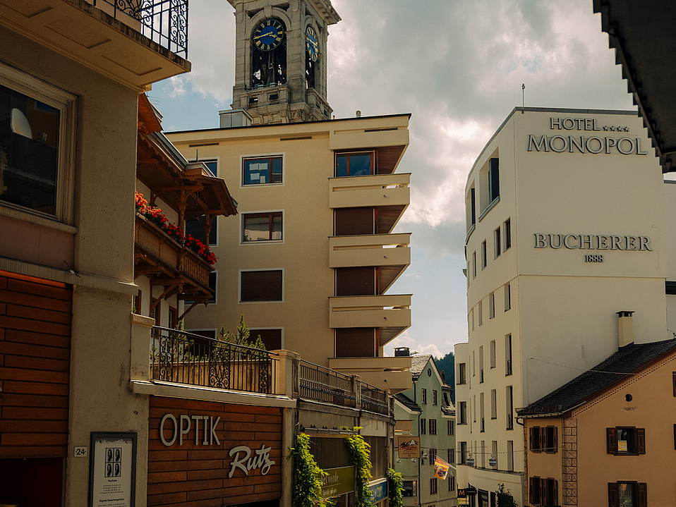 Kirchturm von St. Moritz und Gebäude Kirchturm von St. Moritz, eingerahmt von Gebäuden vor wolkigem Himmel