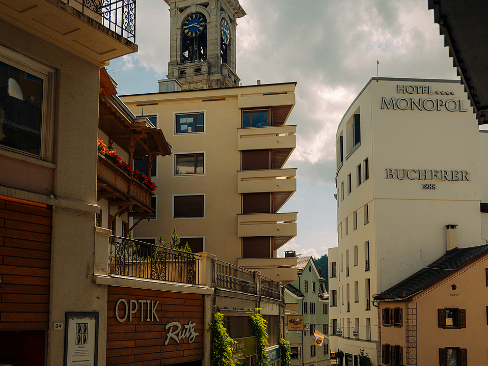 Kirchturm von St. Moritz und Gebäude Kirchturm von St. Moritz, eingerahmt von Gebäuden vor wolkigem Himmel