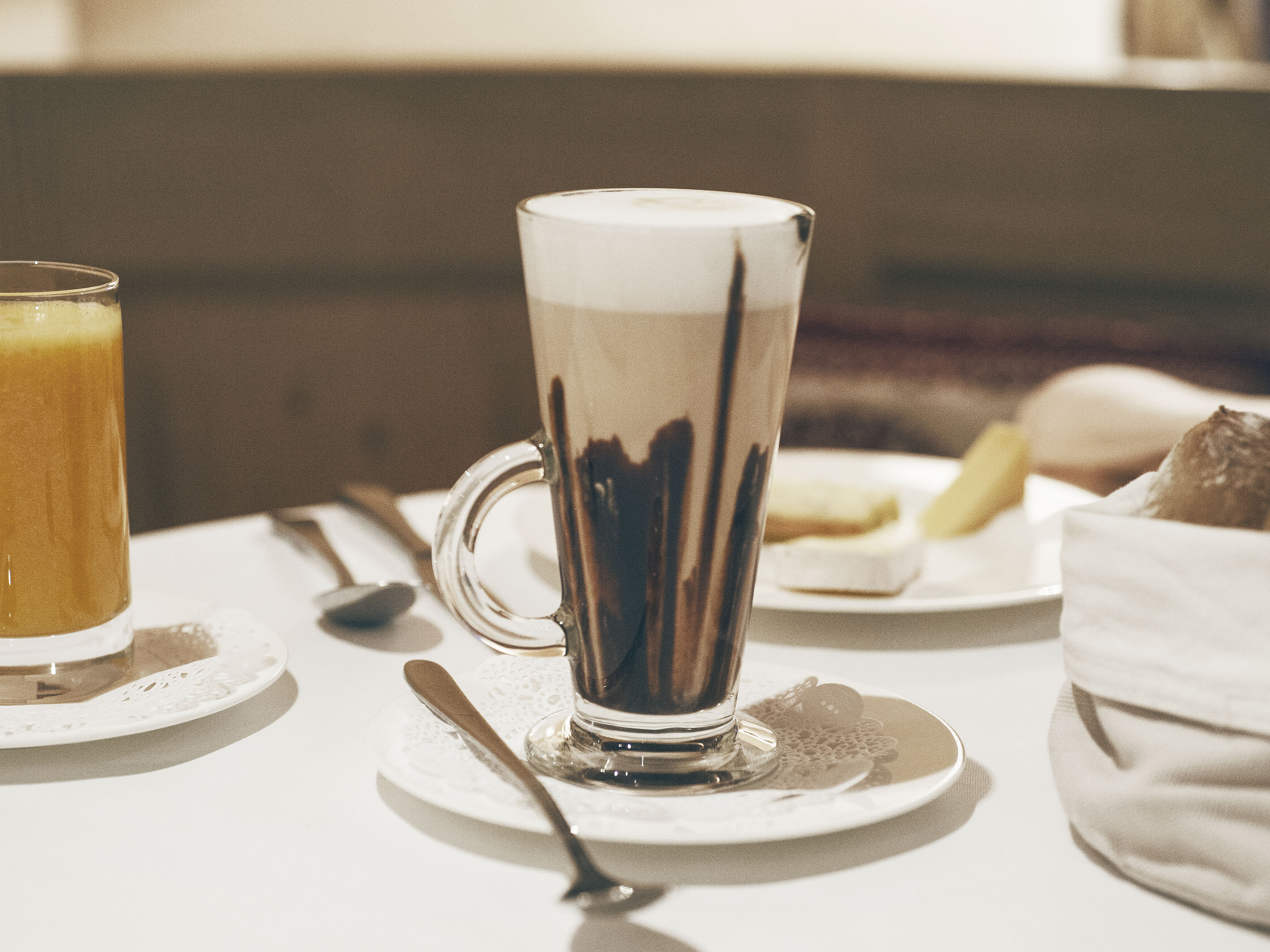 Latte Macchiato mit Schokosirup Hohes Glas Latte Macchiato mit Schokosirup auf weißem Tisch