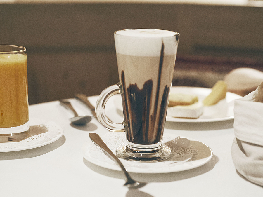 Hohes Glas Latte Macchiato mit Schokosirup auf weißem Tisch