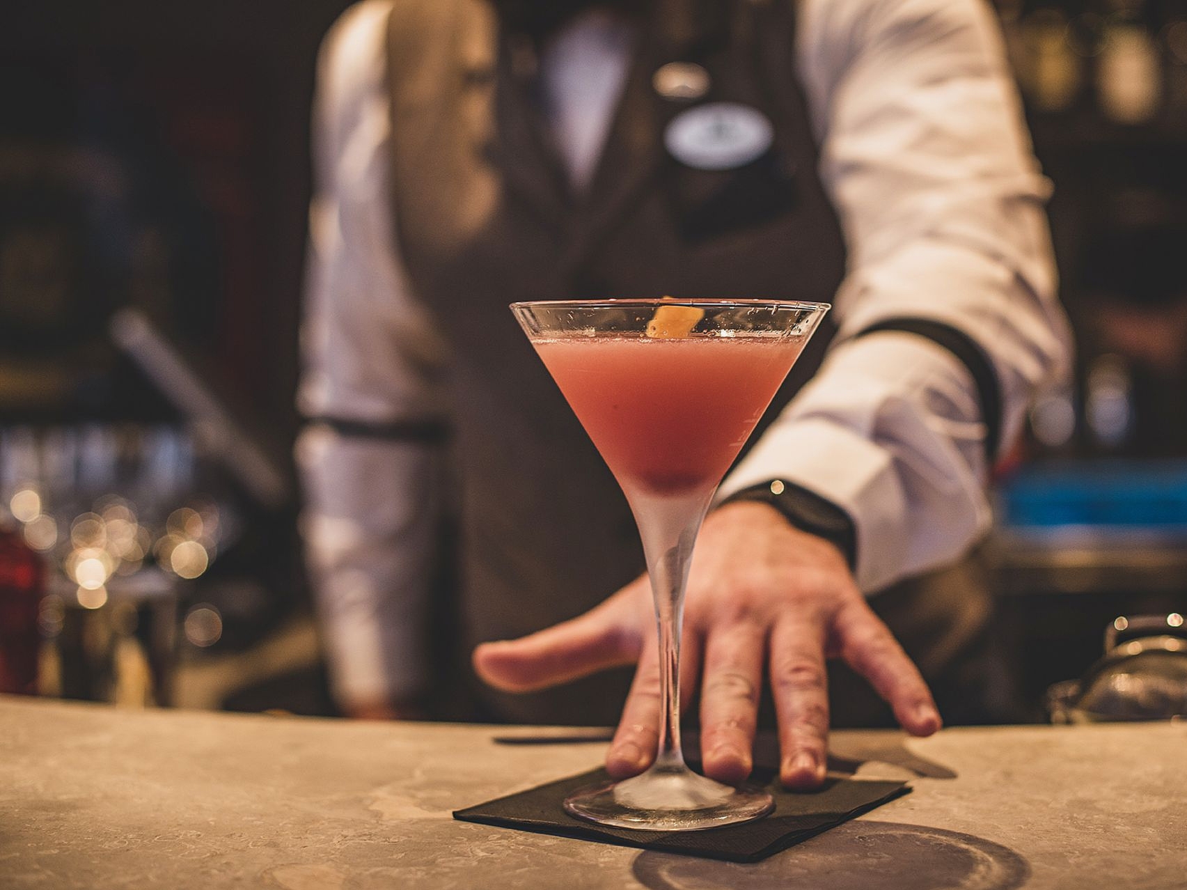 Cocktail am Bartresen Ein rosa Cocktail in einem Martiniglas, serviert von einem Barkeeper.