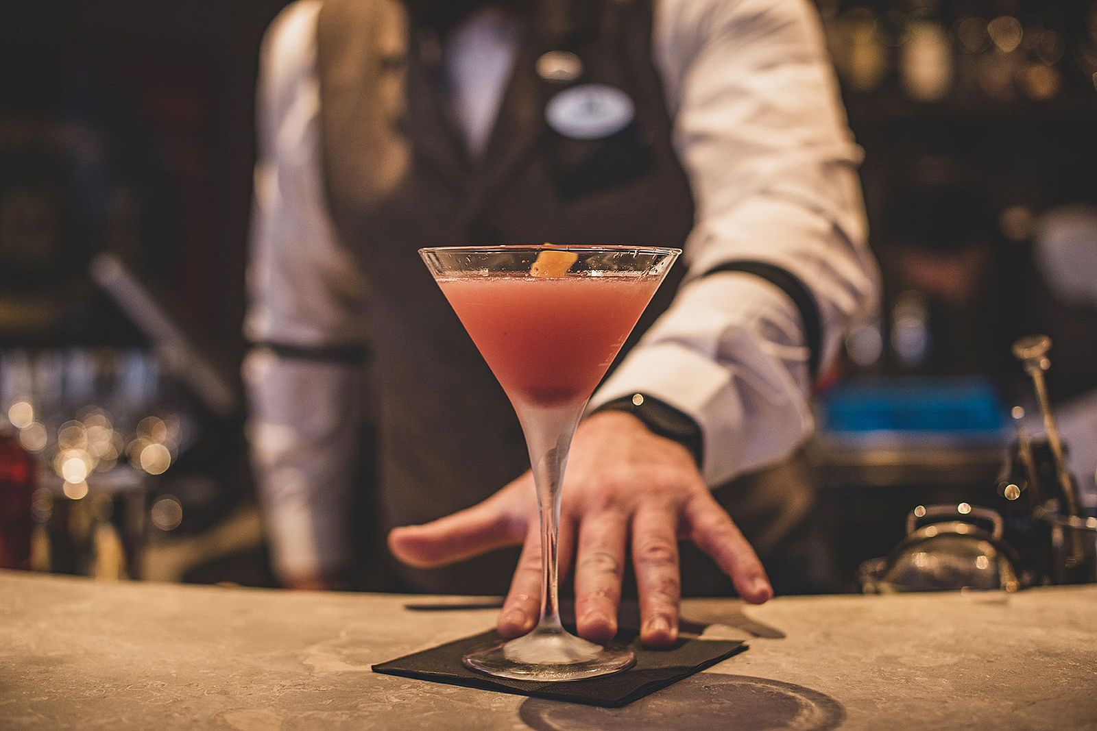 Ein rosa Cocktail in einem Martiniglas, serviert von einem Barkeeper.